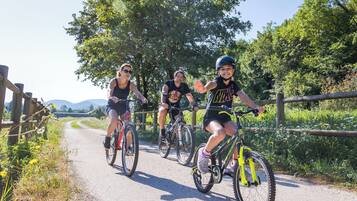 Tres ciclistas en un camino de grava con una valla de madera a un lado y árboles al fondo.