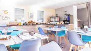 Een moderne eetruimte met tafels en stoelen, een keukenhoek en een aanrecht met een koffieapparaat.