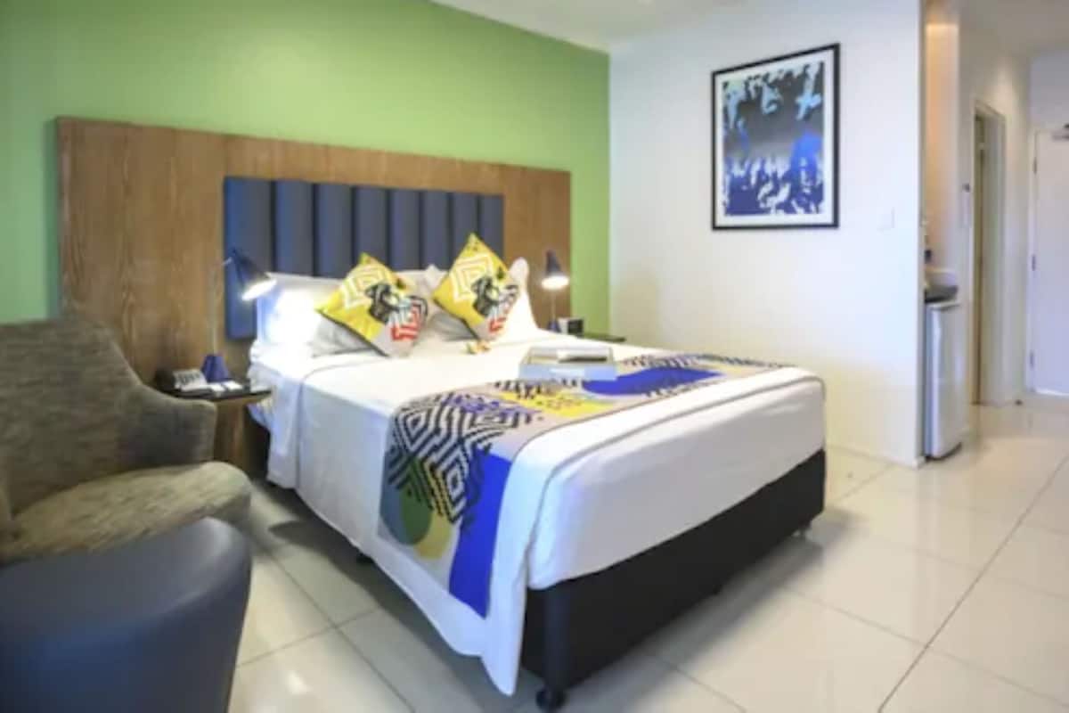 Una habitación de hotel con cama, una silla, una mesita de noche y un cuadro colgado en la pared.