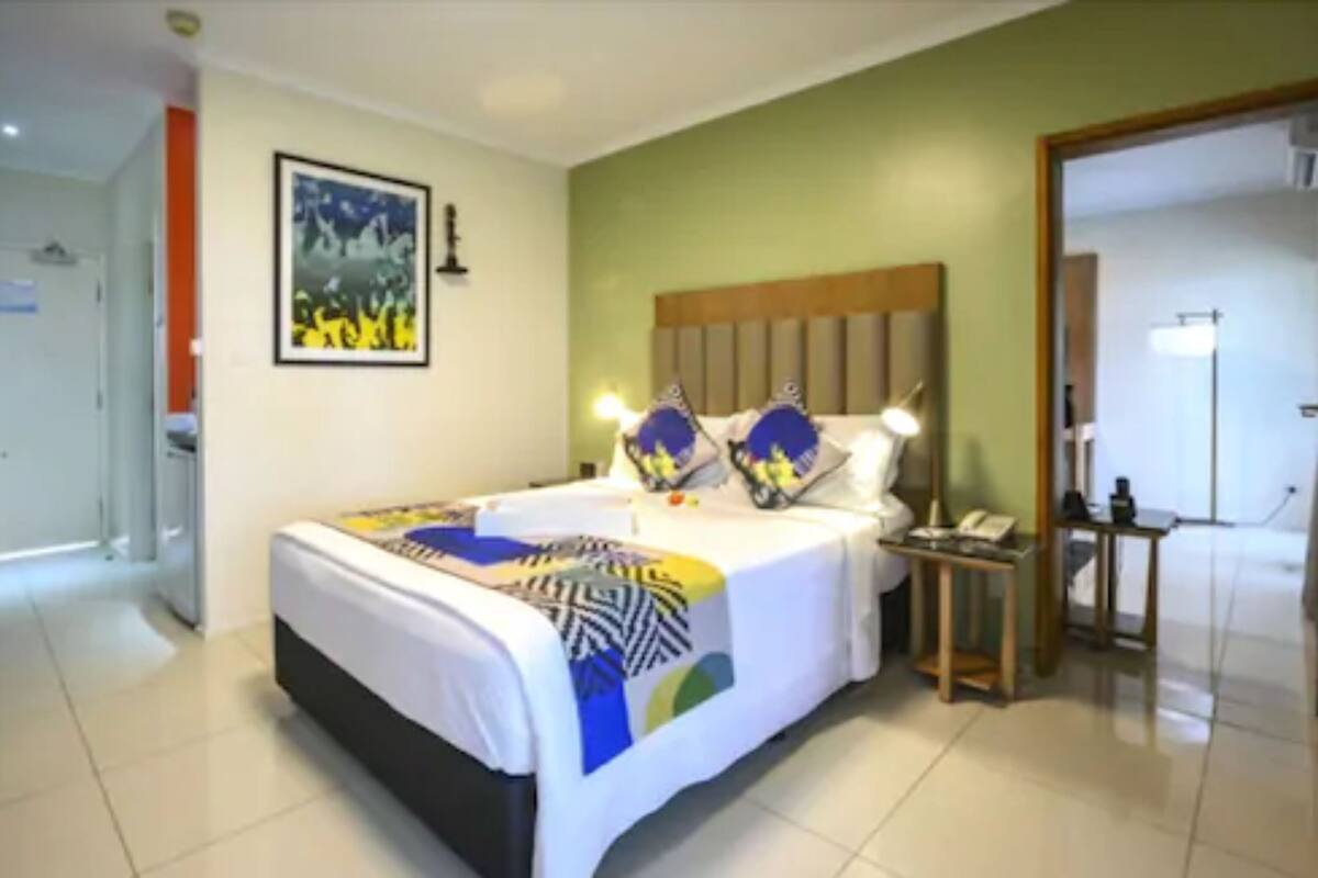 Una habitación de hotel con una cama, mesitas de noche, un espejo y una puerta.