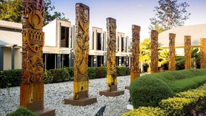 Una serie de pilares de madera tallados con intrincados diseños en un jardín ajardinado, con un edificio al fondo.