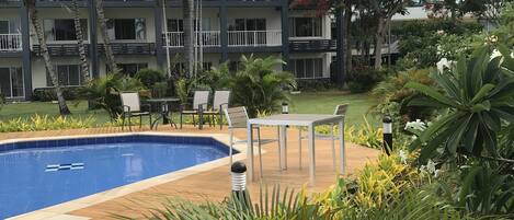 A hotel with a swimming pool, palm trees, and a red flowering tree.