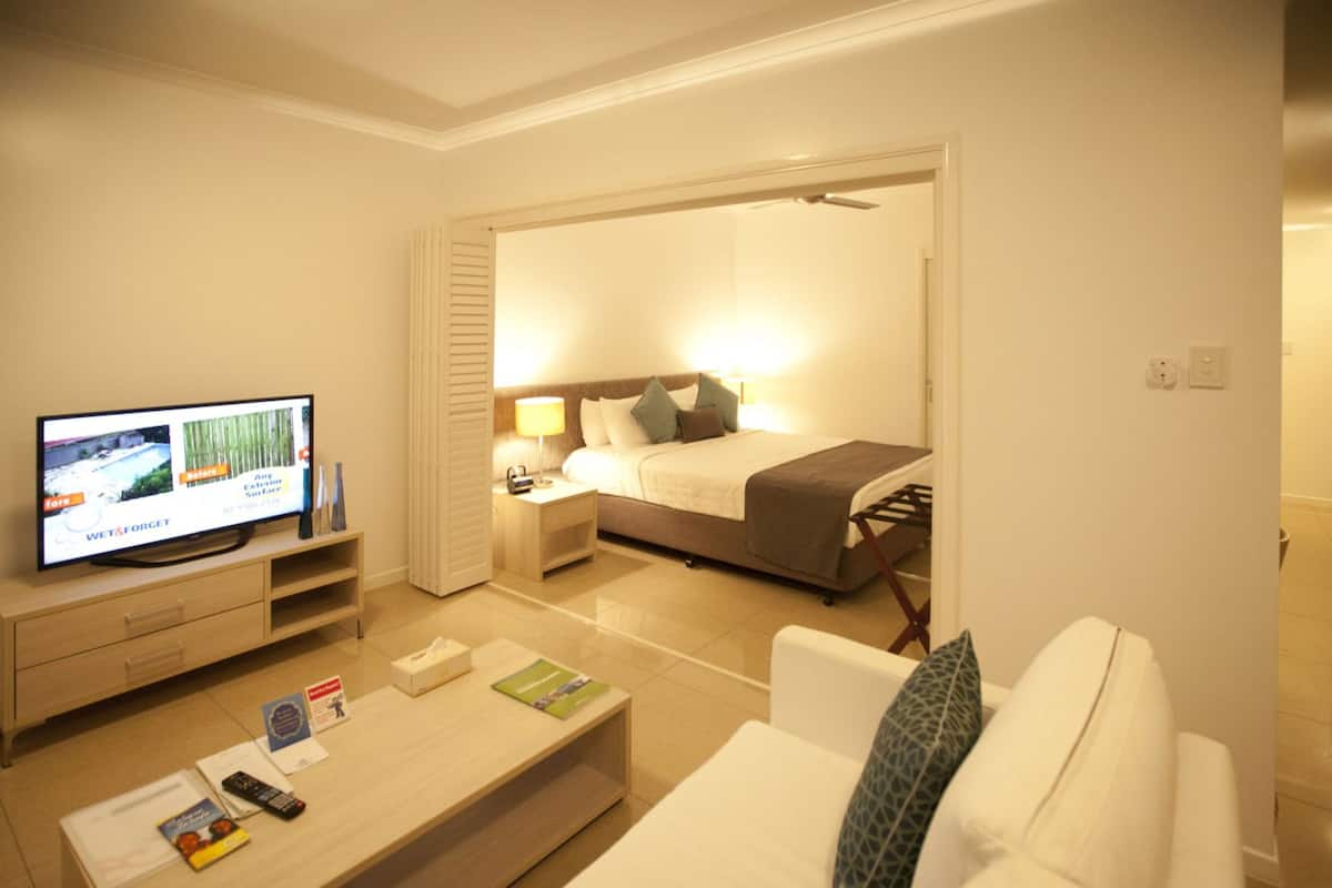 Habitación de hotel con televisión, sofá, mesa de centro, cama y mesita de noche.
