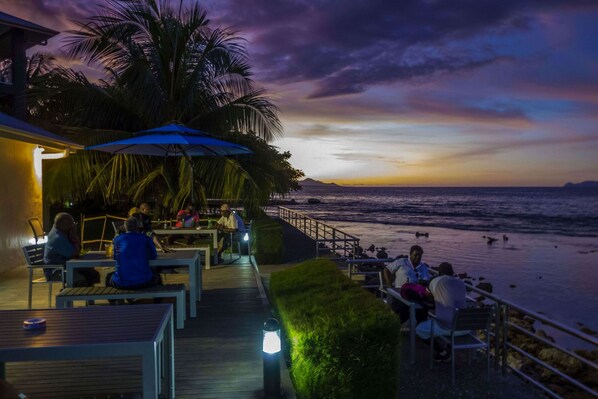 A seaside restaurant with outdoor seating overlooking the ocean, featuring tables and umbrellas. - Heritage Park Hotel (Honiara)