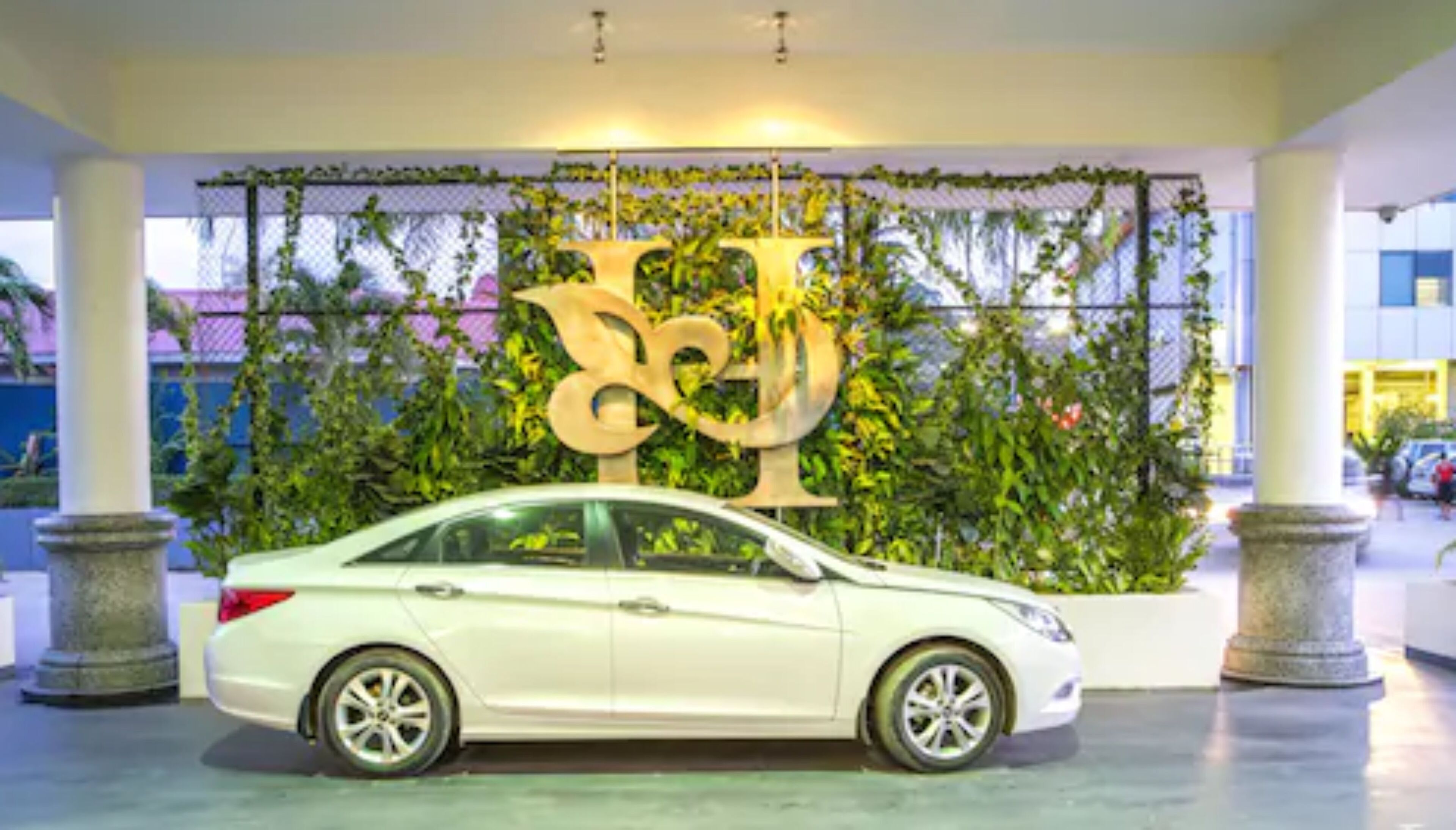 Une voiture blanche est garée devant un immeuble orné d’une grande enseigne décorative.