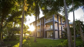 Un hotel de varios pisos con balcones, rodeado de palmeras y un césped cuidado.