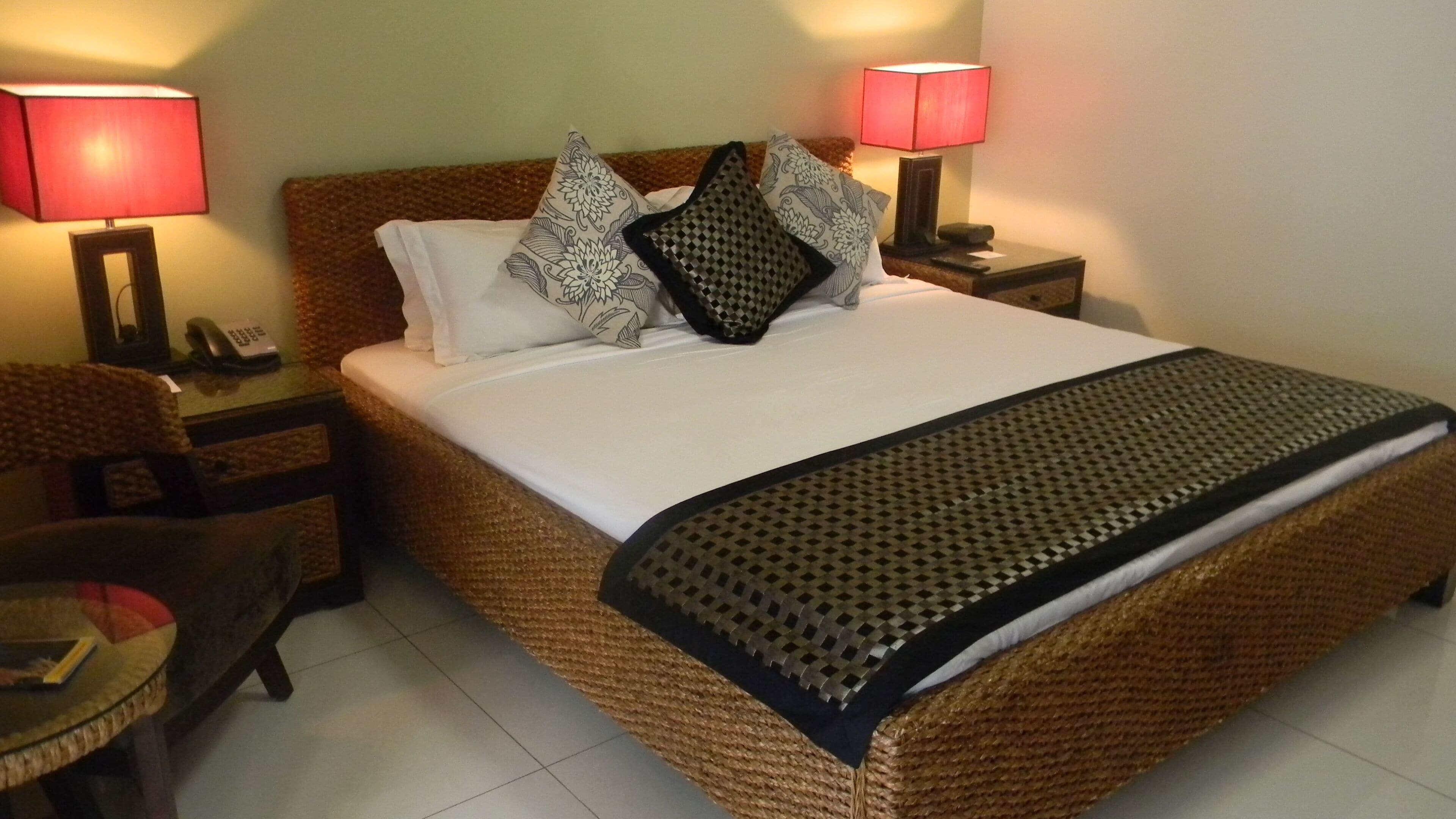 Una cama bien hecha con una manta estampada, dos lámparas de noche, un teléfono y una silla.