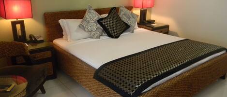 Una cama bien hecha con una manta estampada, dos lámparas de noche, un teléfono y una silla.
