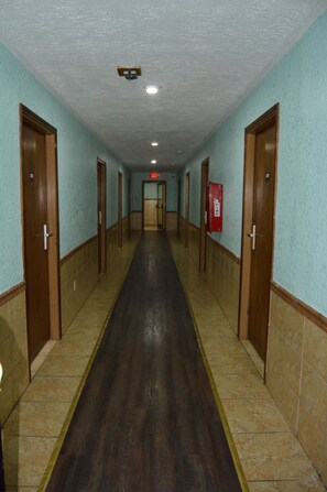 A long, narrow hallway with doors on both sides, a fire extinguisher on the right wall, and a light at the end. - Budget Inn of Claypool Hill (Pounding Mill)
