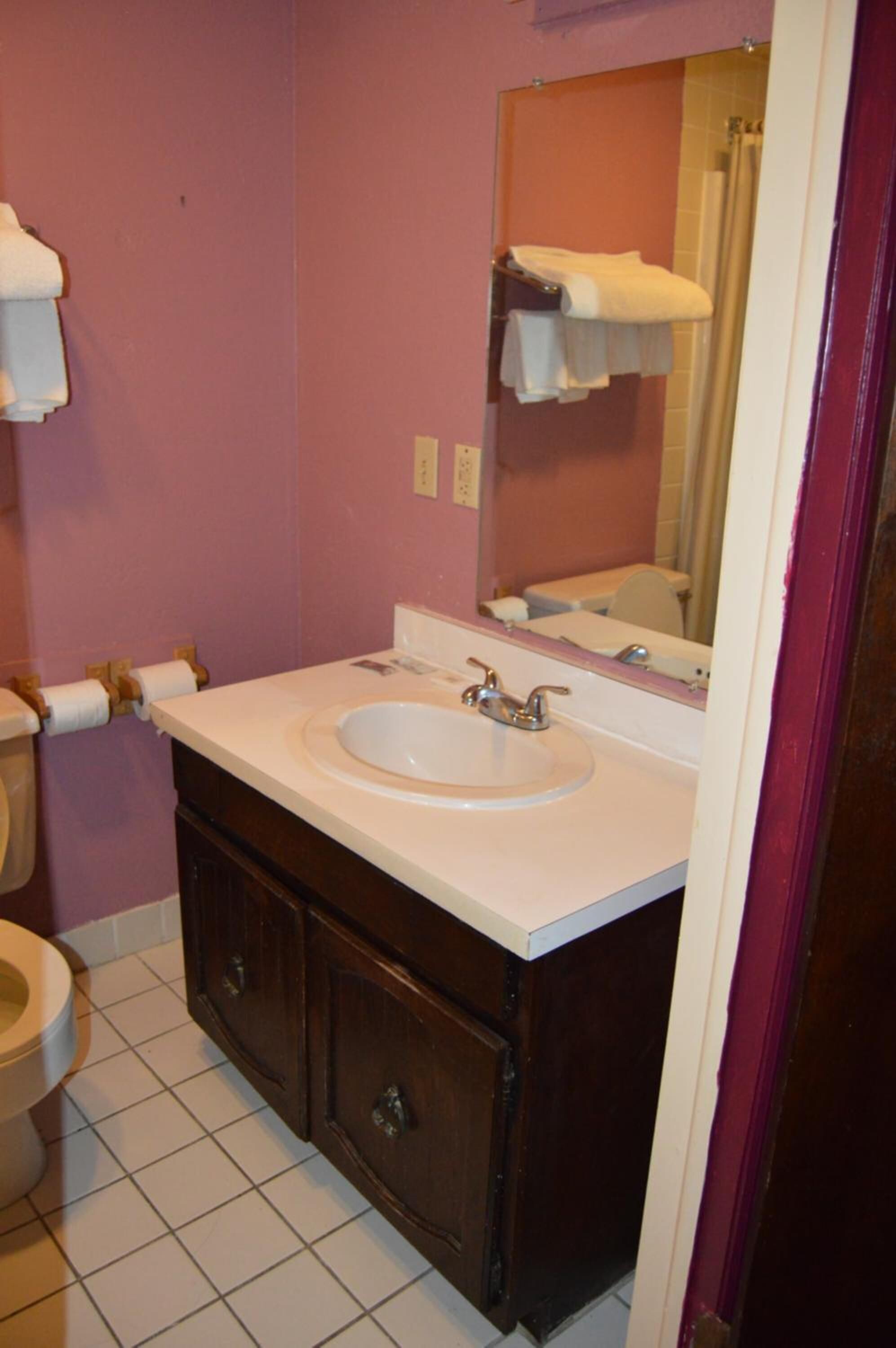 A bathroom with a white sink, dark wooden cabinets, a mirror, and a toilet.
