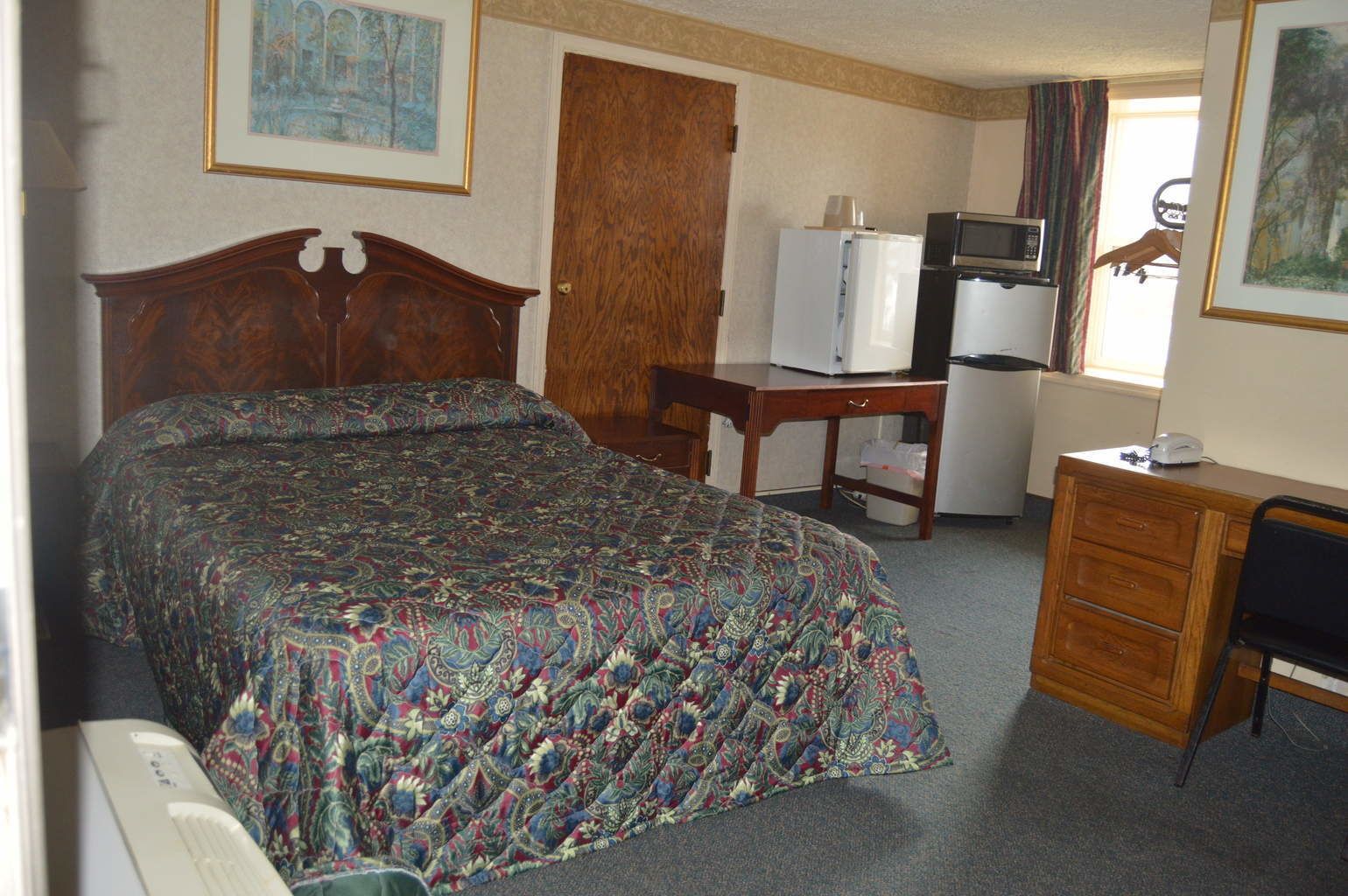 A hotel room with a bed, a desk, a dresser, a television, and a refrigerator.