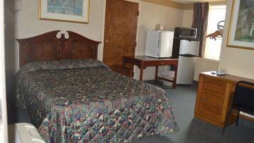 A hotel room with a bed, a desk, a dresser, a television, and a refrigerator.