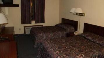 Una habitación de hotel con dos camas, un escritorio, una lámpara y un televisor sobre una estantería.