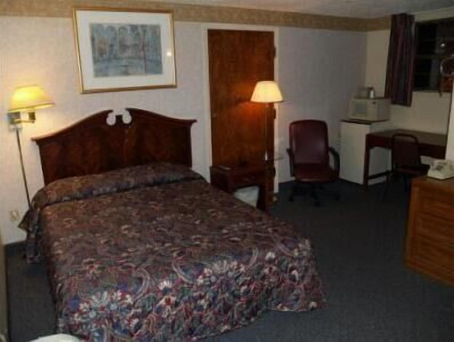 A hotel room with a large bed, a desk, and two chairs.
