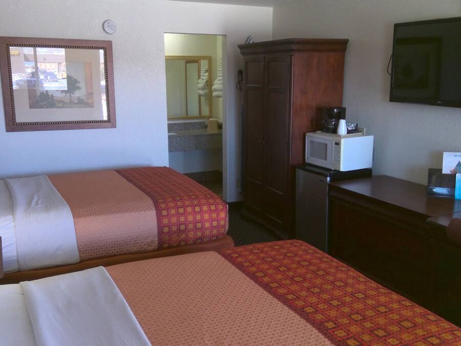 A hotel room with two beds, a desk, a microwave, a television, and a mirror.