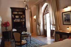 A hotel room with a large window, a bookshelf, a desk with a lamp, a chair, and a bed. - Demeures d'orient Riad Deluxe & Spa (Marrakech)