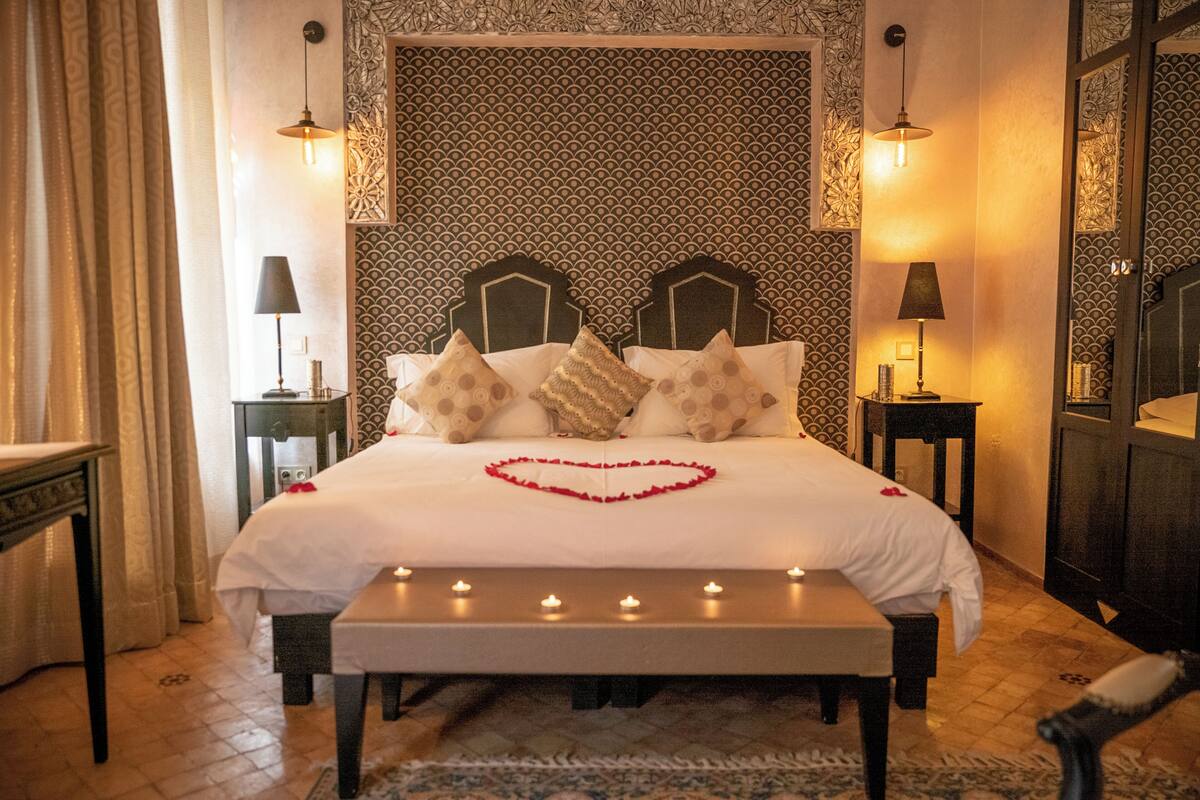 A hotel room with a large bed, two bedside tables, a bench, and a patterned wall.
