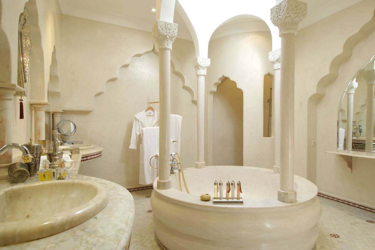 A luxurious bathroom with a large bathtub, a round sink, and ornate columns.