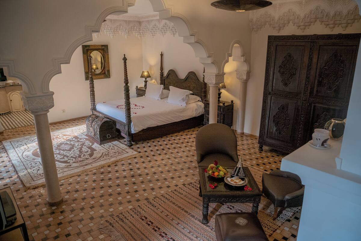 A traditional Moroccan room with a four-poster bed, ornate furniture, and a patterned floor.