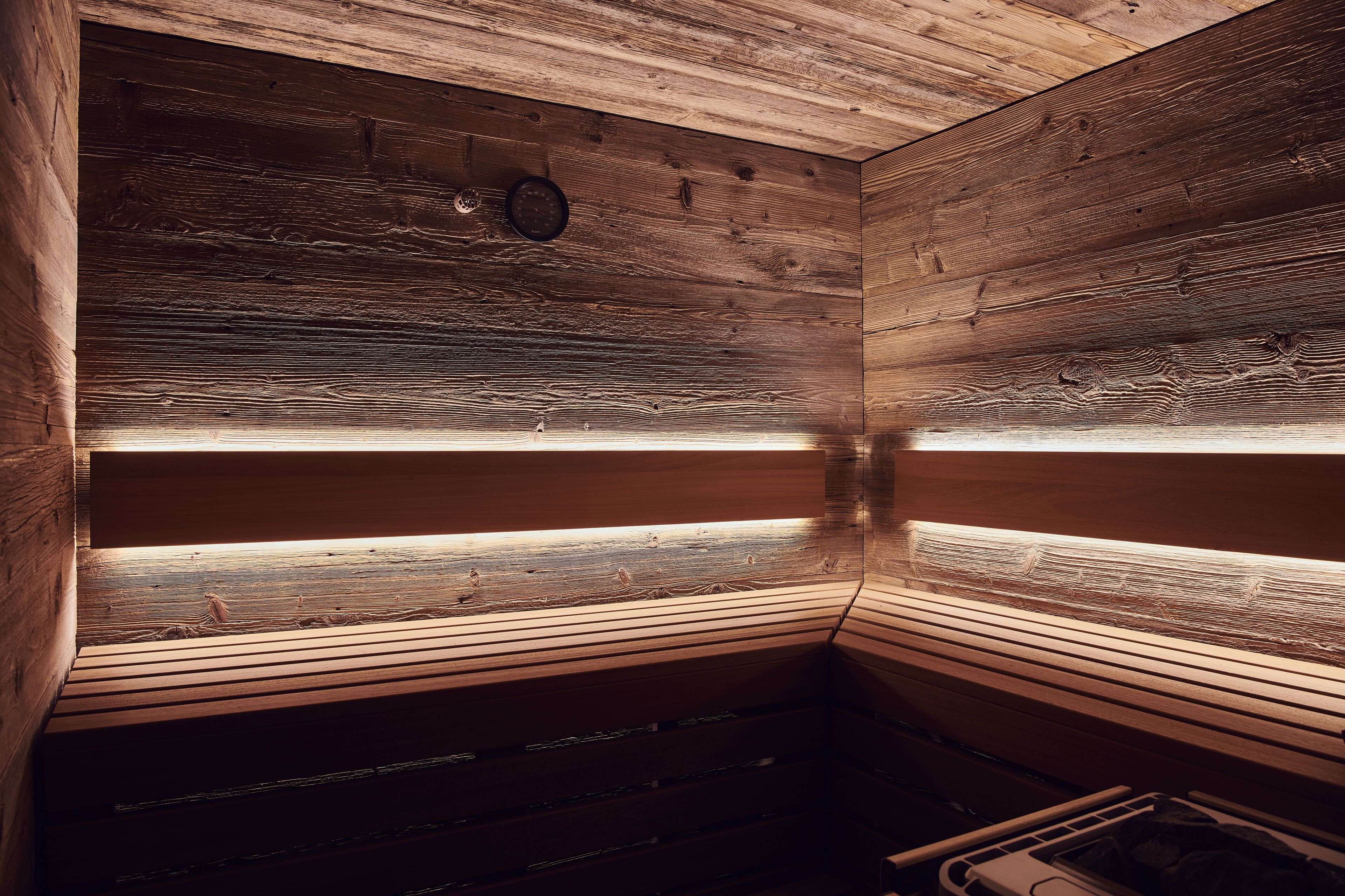 Un sauna avec des murs et des bancs en bois, une barre de maintien visible et une petite fenêtre.