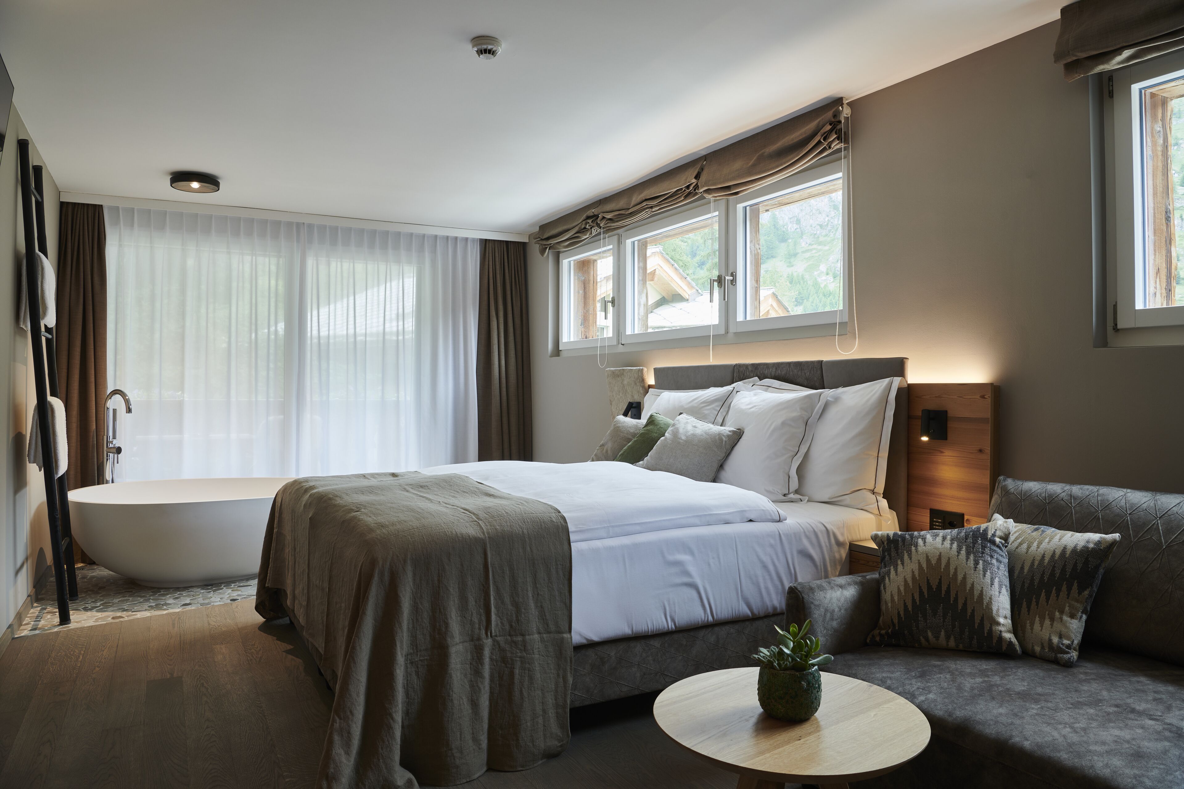 A modern bedroom with a large bed, a sofa, a round coffee table, and a bathtub.