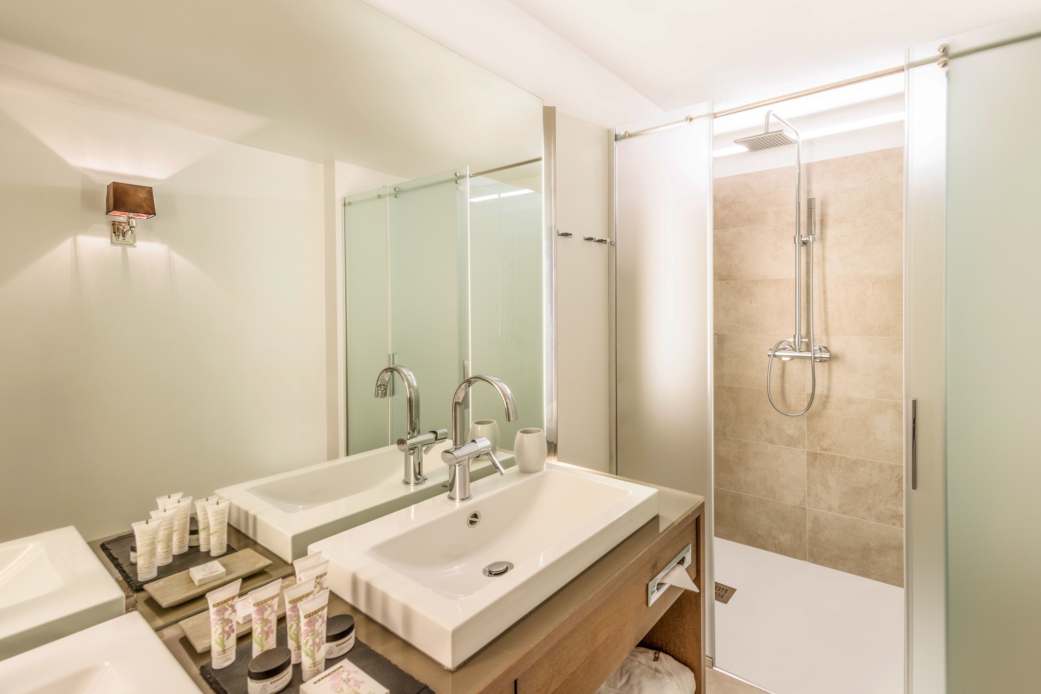 Ein modernes Badezimmer mit zwei Waschbecken, einer Duschkabine aus Glas und einem Spiegel über den Waschbecken.
