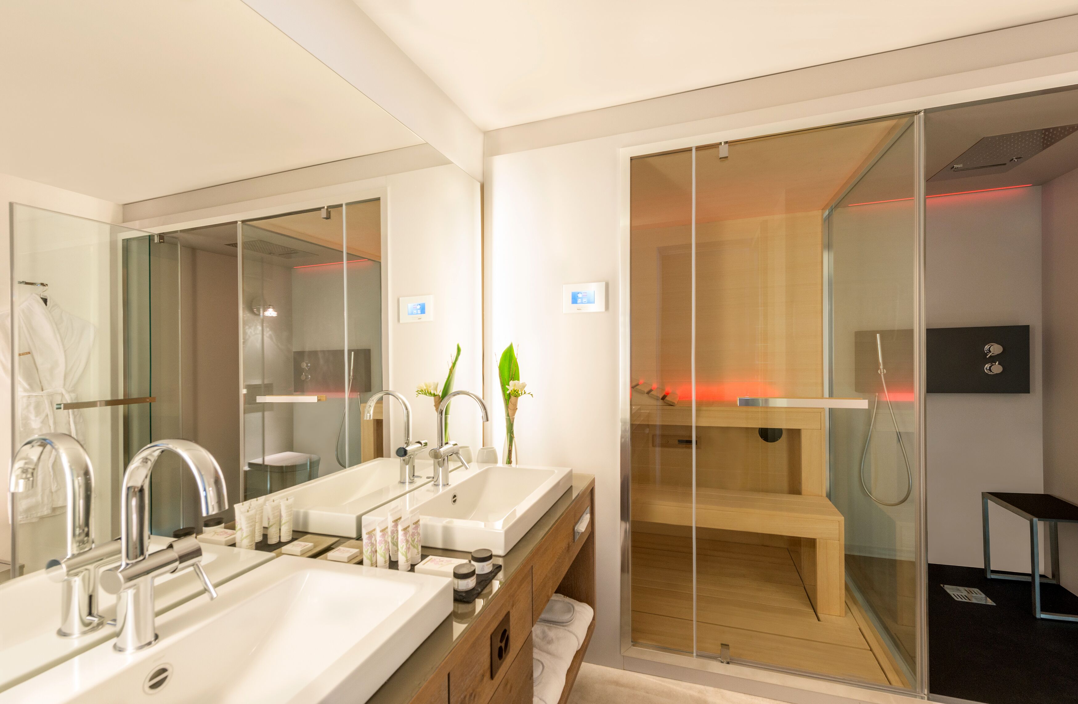 A modern bathroom with dual sinks, a large mirror, a glass-enclosed shower, and a wooden bench.