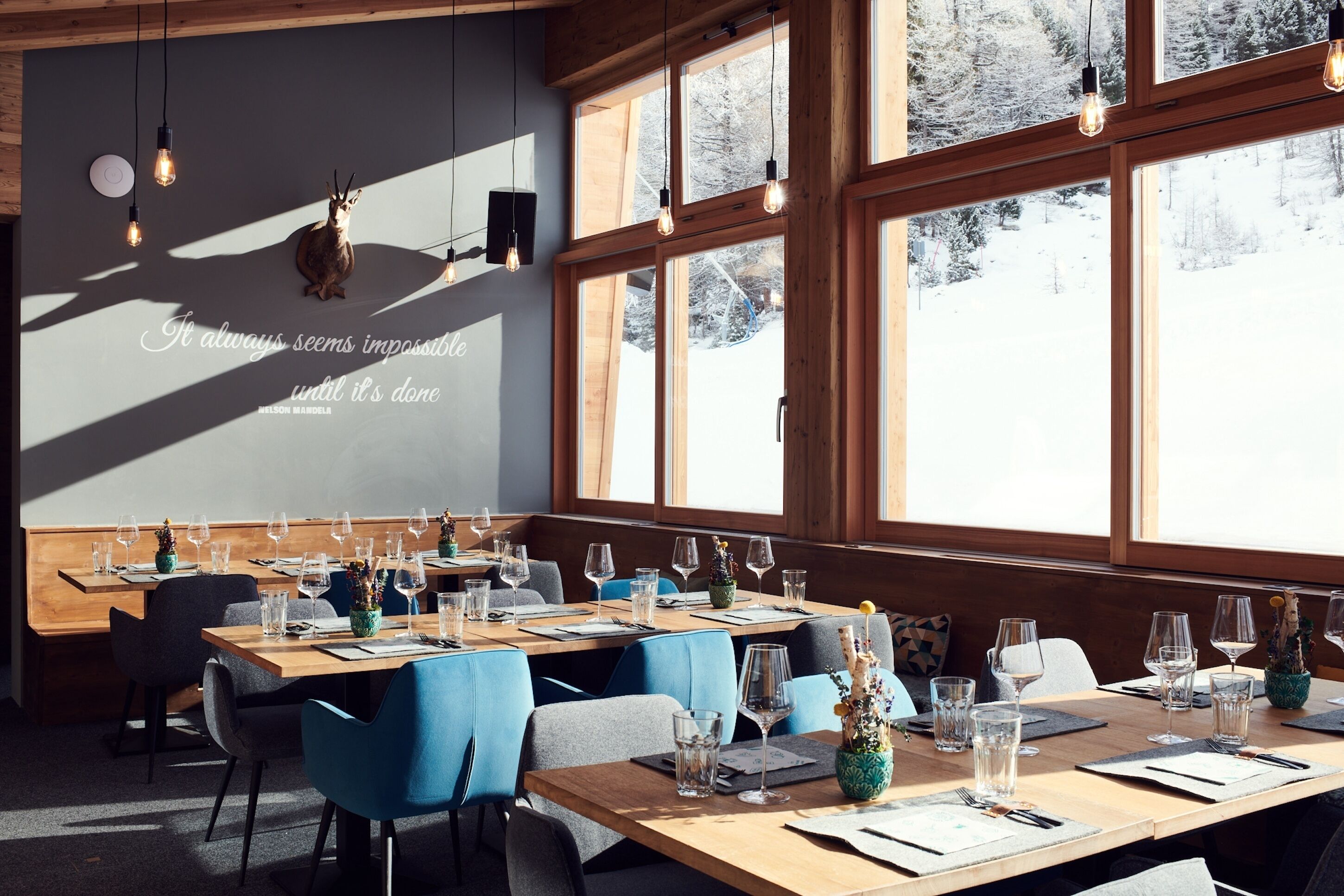 A dining area with wooden tables, blue chairs, and large windows with a snowy view.