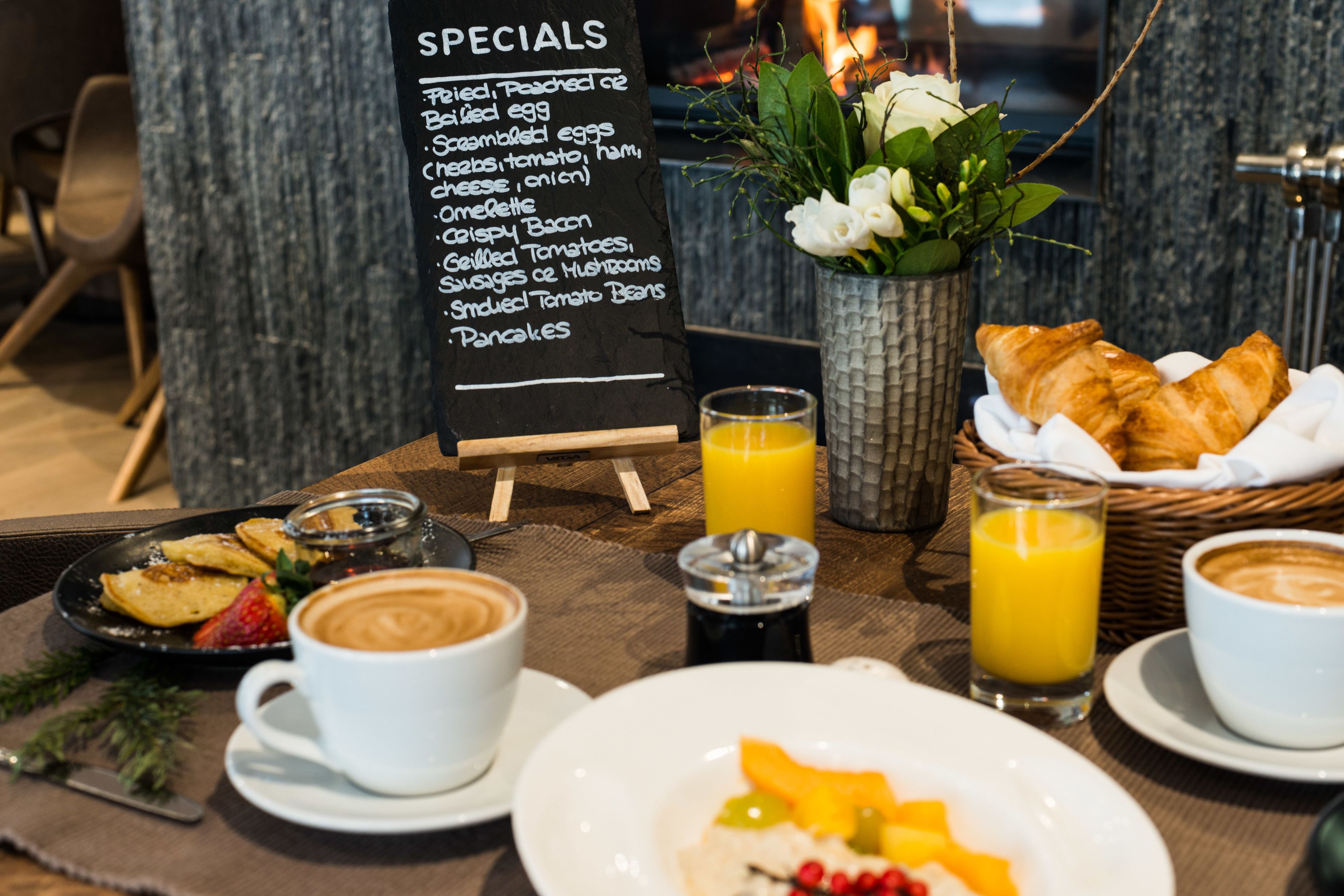A breakfast setup with a menu board, croissants, fruit, coffee, and juice.