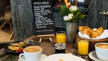 A breakfast setup with a menu board, croissants, fruit, coffee, and juice.