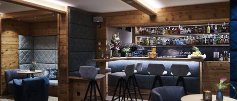 Zona de bar con vigas de madera, taburetes y una variedad de botellas de licor.