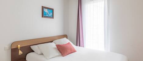 A neatly made bed with white and pink pillows, a wooden headboard, and a small bedside table with a lamp.