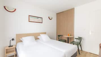 A hotel room with a double bed, a bedside table with a lamp, a small round table with chairs, and a wardrobe.