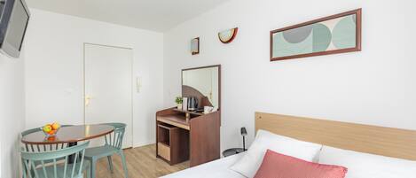 Habitación de hotel con cama, escritorio, silla, televisor y una mesita con fruta.