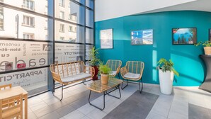 A modern indoor seating area with wicker chairs and a table, large windows, and a teal accent wall. - Appart’City Confort Brest (Brest)