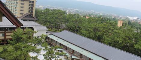 A traditional Japanese building with a sloped roof, surrounded by lush greenery and a view of distant mountains.