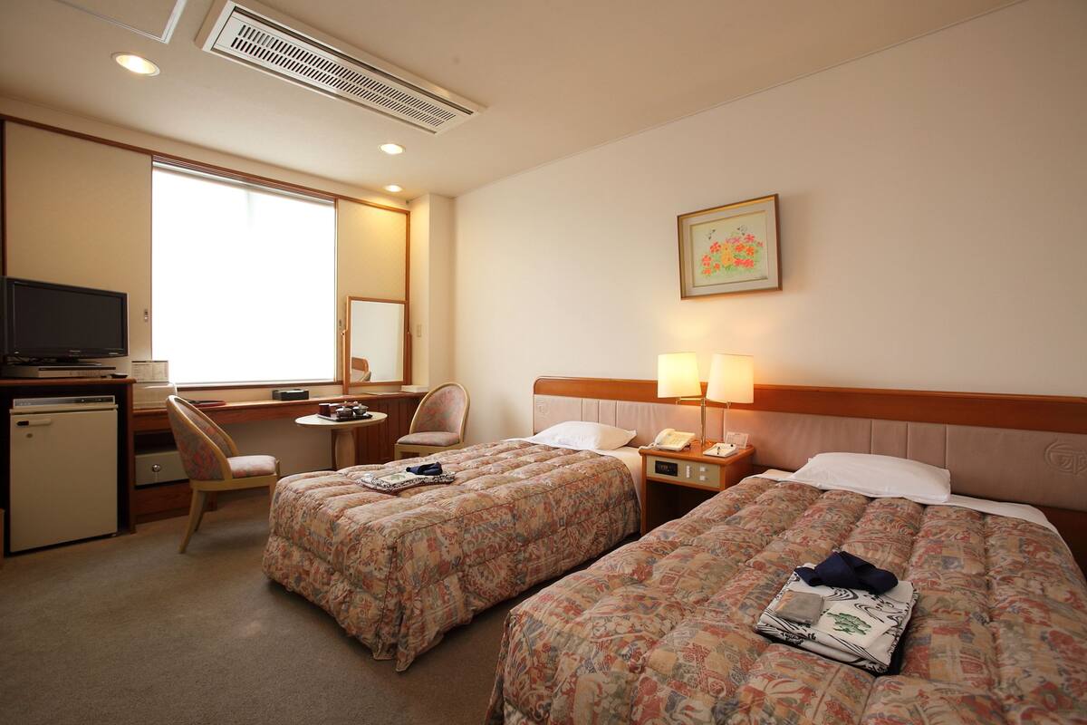 Habitació d'hotel amb dos llits, un escriptori, una cadira, una televisió i una finestra.