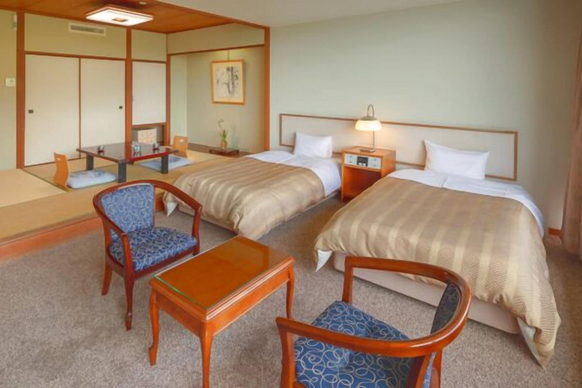 Habitació d'hotel amb dos llits, una taula petita, dues cadires, una tauleta de nit i un mirall.