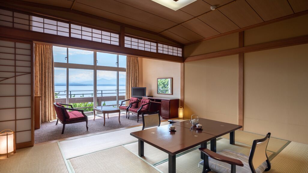 A traditional Japanese room with tatami flooring, a low table with cushions, a TV, and a view of the sea.