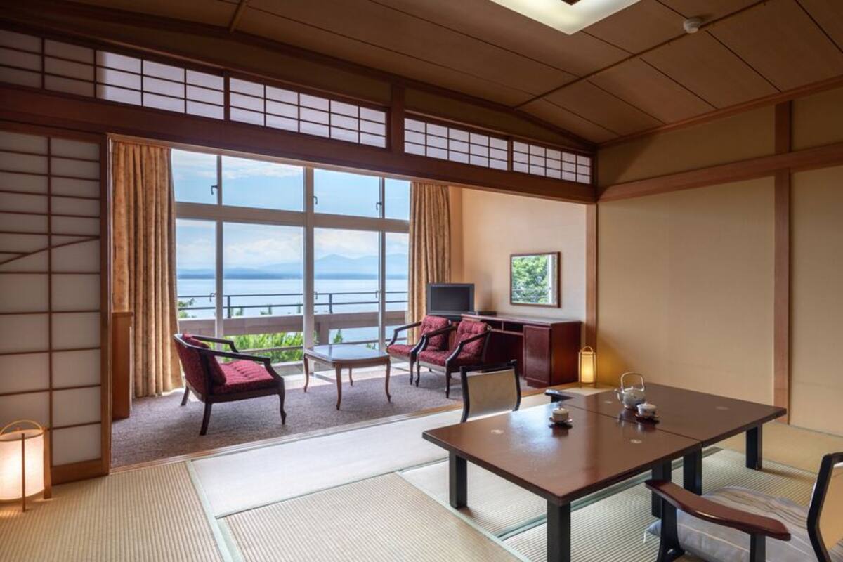 Habitació japonesa tradicional amb sòl de tatami, una taula baixa amb coixins, televisió i vista al mar.