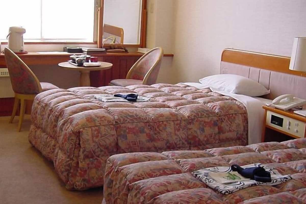 A hotel room with two beds, a desk, a chair, a small table, and a television.