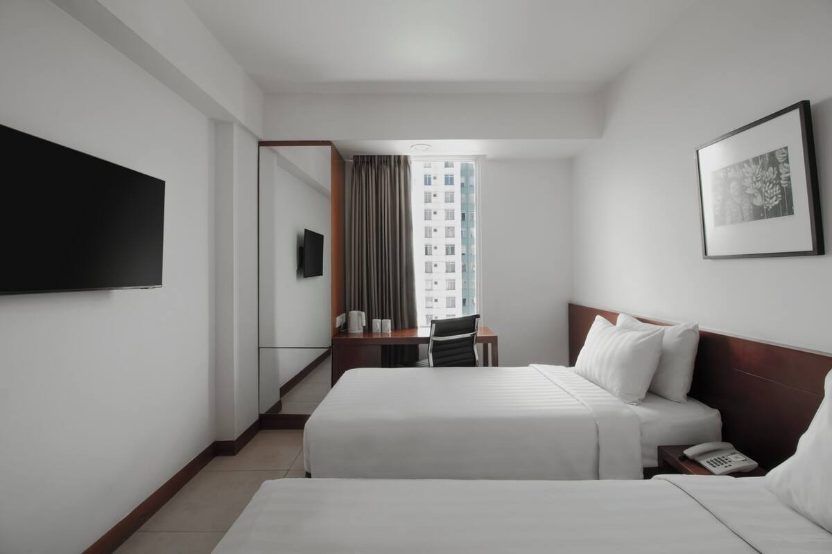 A hotel room with two beds, a desk, a chair, a flat-screen TV, a telephone, and a framed picture on the wall.