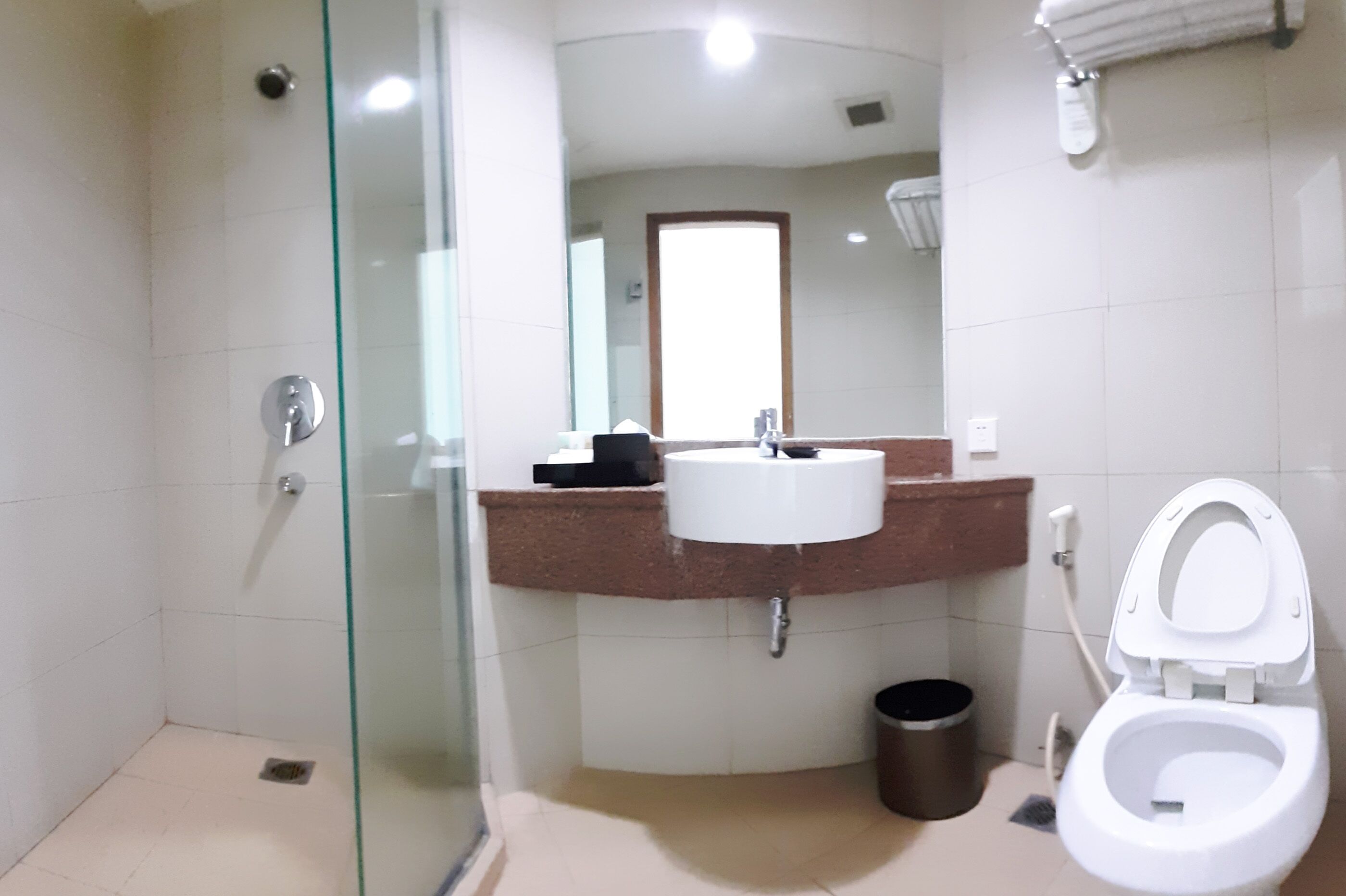 A modern bathroom with a glass-enclosed shower, a white sink with a brown countertop, and a white toilet.
