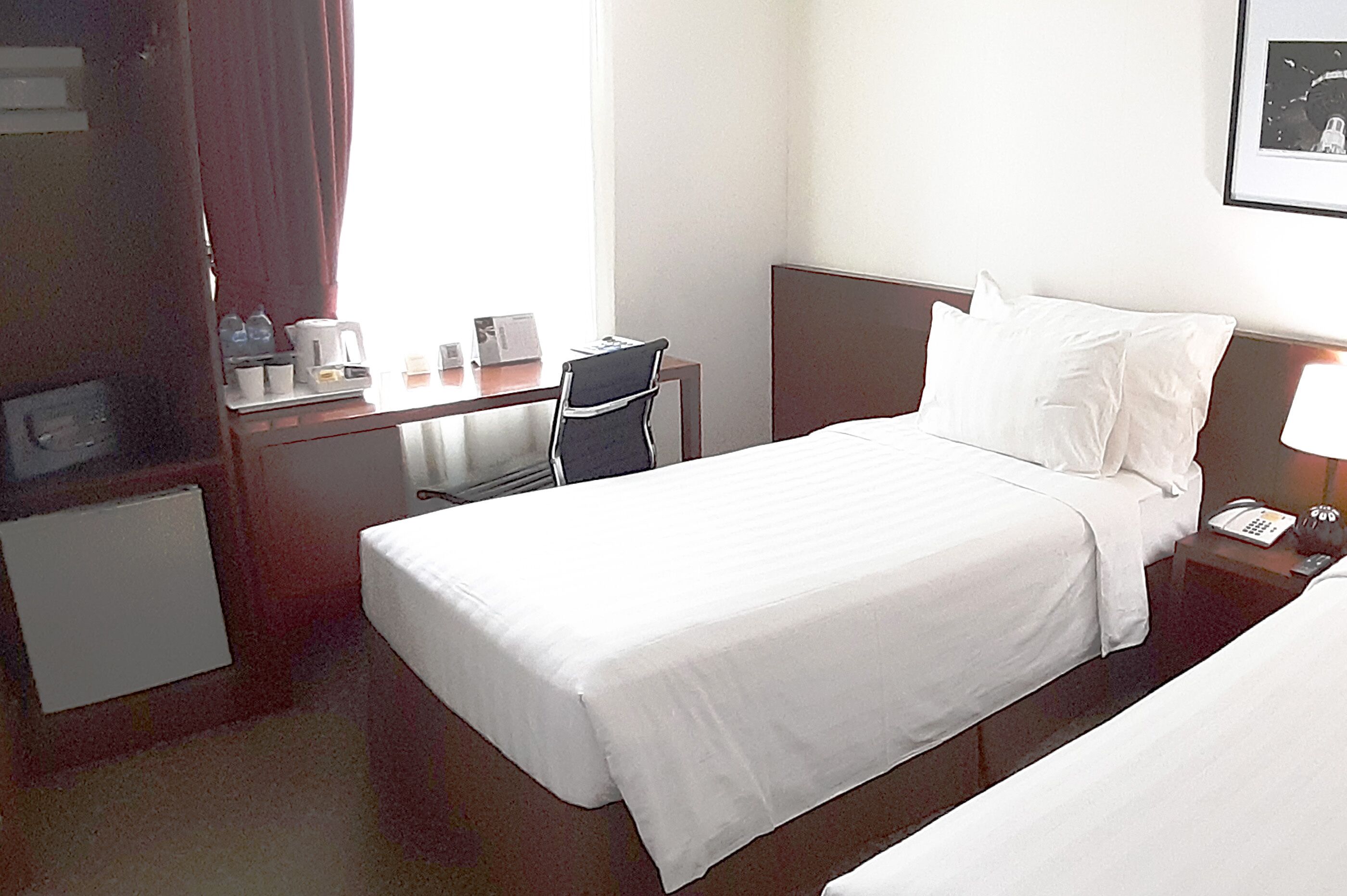A hotel room with a bed, a desk with a chair, a telephone, and a framed picture on the wall.