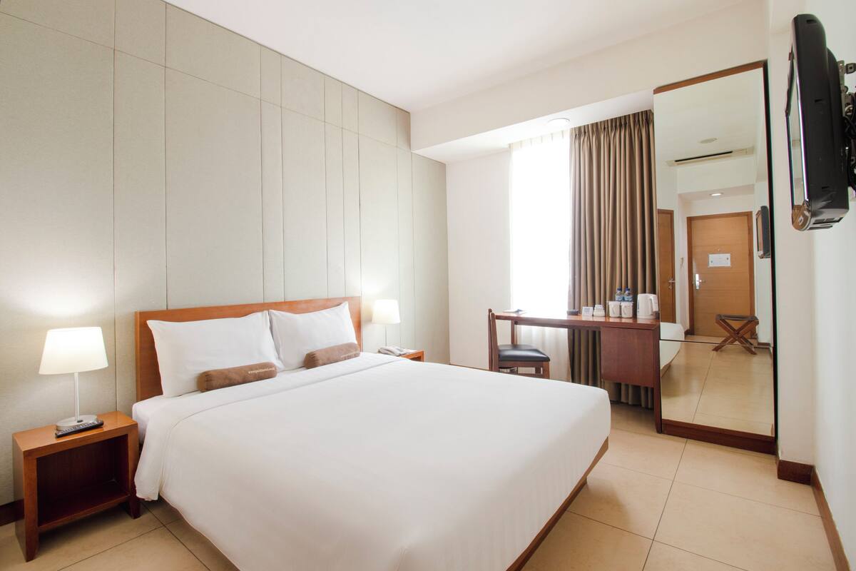 A hotel room with a large bed, bedside tables, a desk, and a mirror.