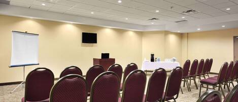 A conference room with rows of chairs, a podium, a projection screen, and a table with water bottles.