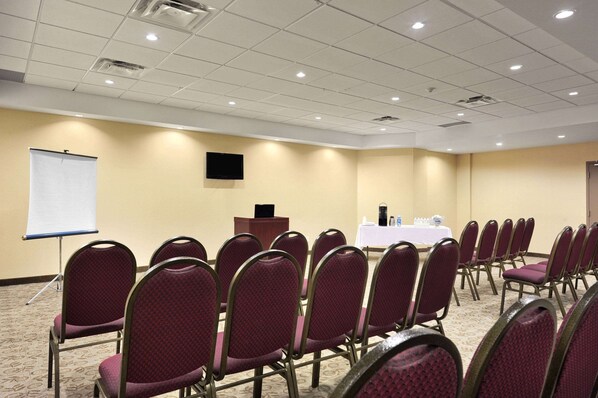 A conference room with rows of chairs, a podium, a projection screen, and a table with water bottles.
