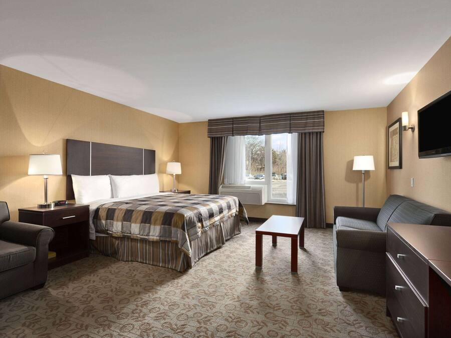 A hotel room with a bed, two bedside tables, a desk, a sofa, and a TV mounted on the wall.