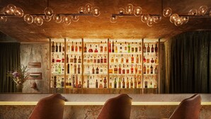 Een bar met houten plafond, flessenrekken en drie gestoffeerde stoelen.