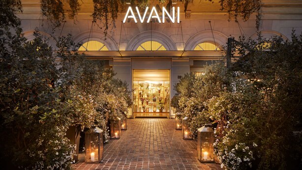 De ingang van hotel AVANI met een met bakstenen bestraat pad, verlicht door lantaarns, omgeven door weelderige begroeiing.